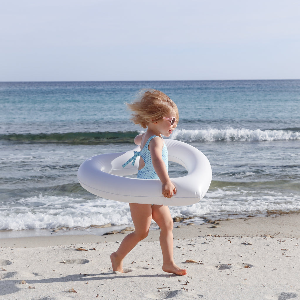Child running with mini white heart shaped float for kids. She is on the beach, running to the right