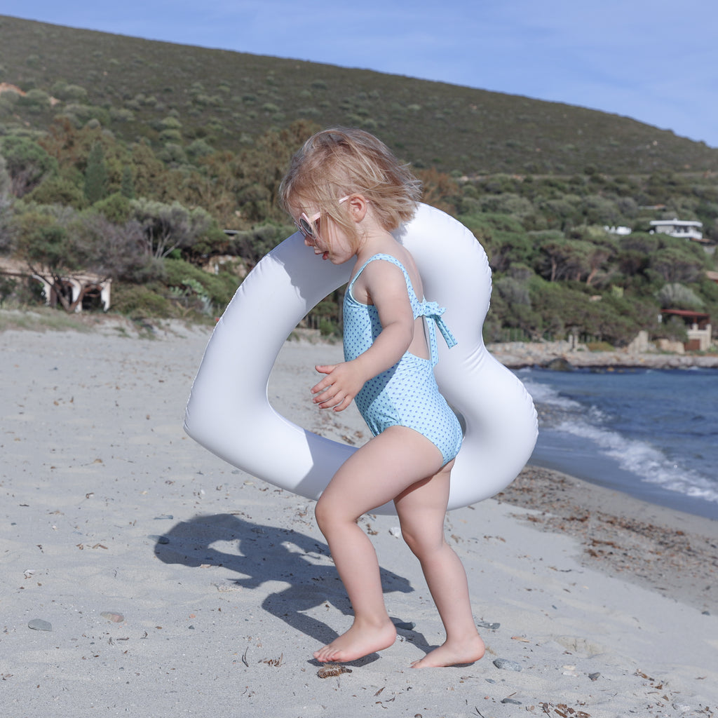 little girl walking away from the water holding the mini white heart shaped pool float on shoulder