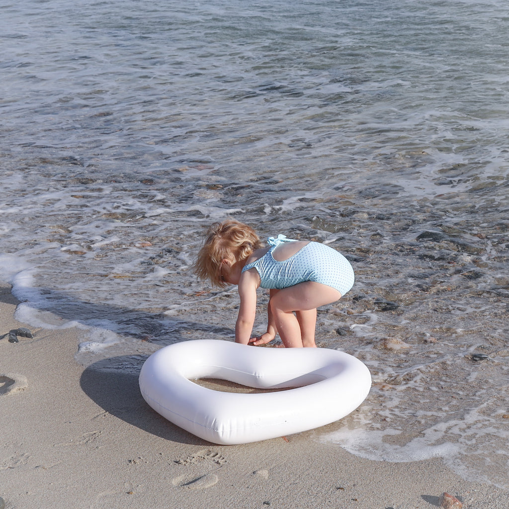 Girl playing in the water next to her mini white heart pool float