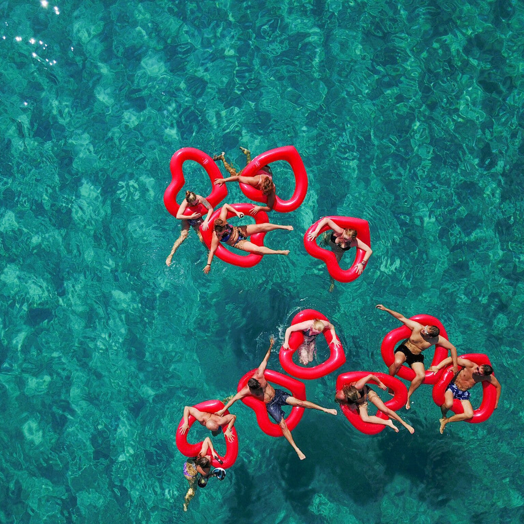 Ariel photo of eleven people in the sea with ten red heart shaped floats from Lôteli 