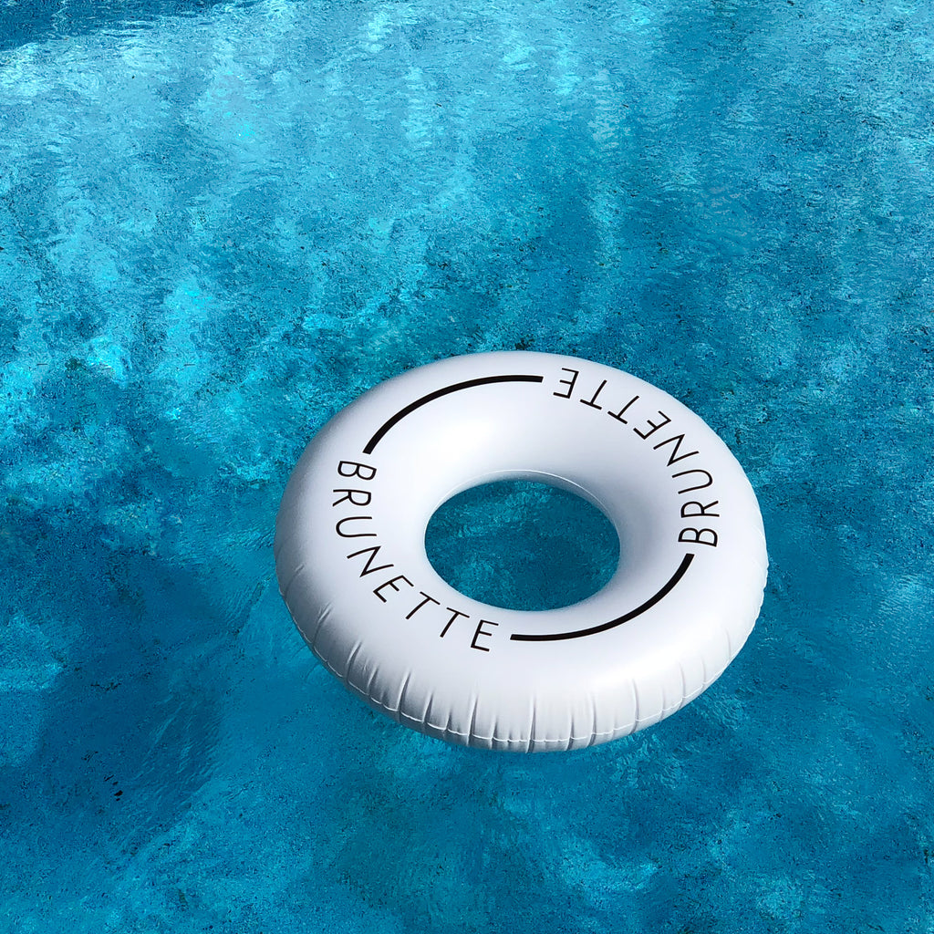 Photo of white swim ring floating in an empty pool. The ring has the word brunette on it. 