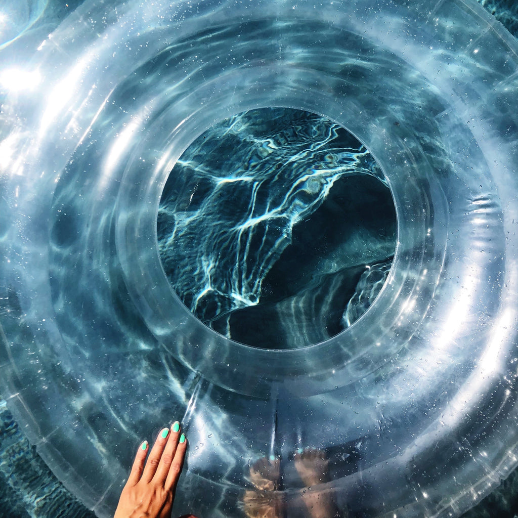 Close up photo of clear swim ring over dark blue water with a hand touching the side of the float.