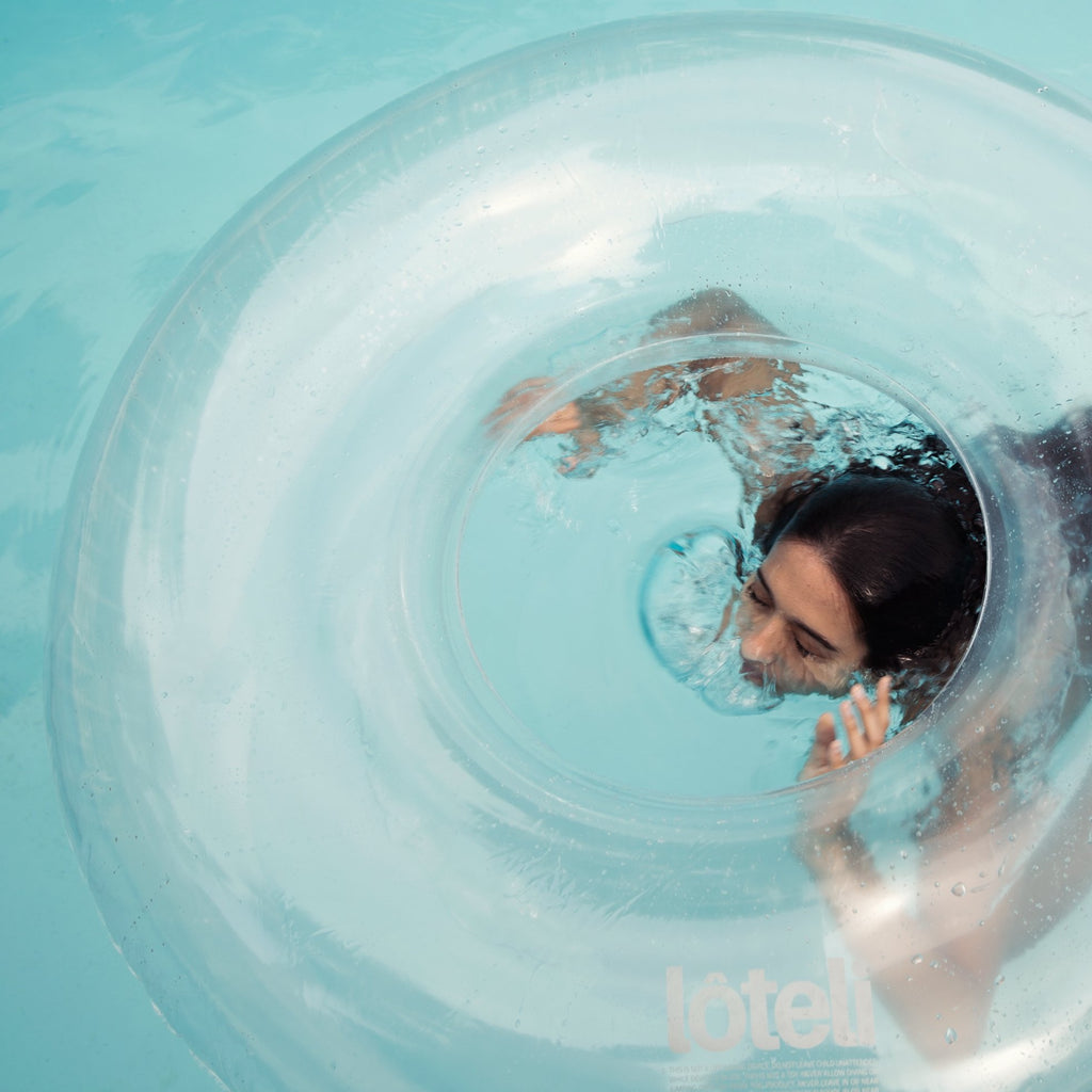 Woman breaking the surface of the pool water under her clear designer swim ring